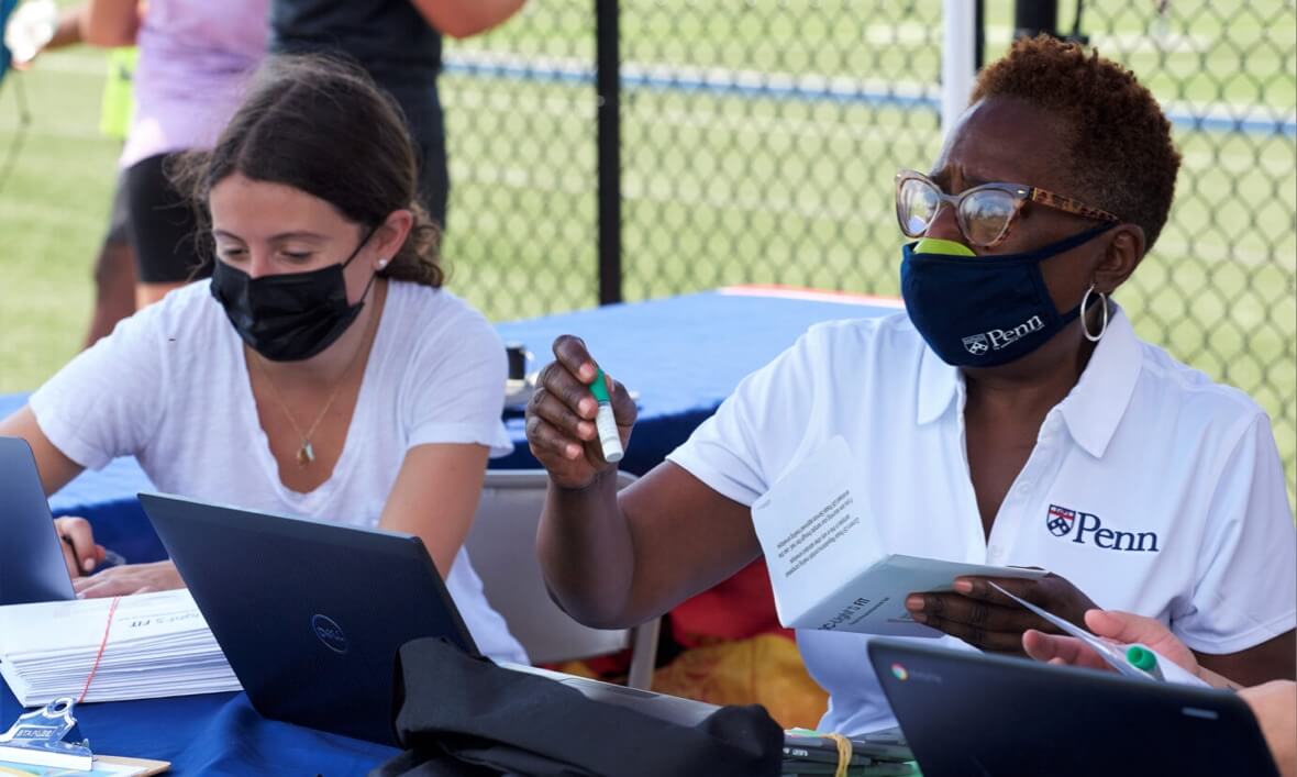 Armenta Washington and a colleague wear masks and sit side by side at a table with laptop computers, helping to coordinate a clinical trial.