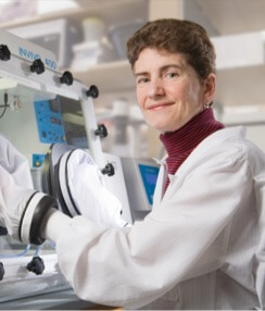 Dr. Celeste Simon sits in a laboratory setting, with her hands in gloves inside a machine.