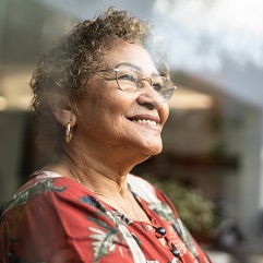 An older woman smiles and looks toward the sky in an outdoor setting.