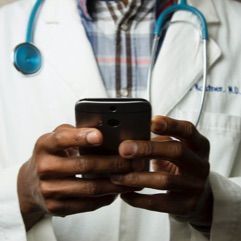 A doctor looks at his cellphone while a stethoscope hangs around his neck.